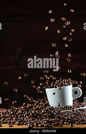 Disposizione dei battenti scuro arrosto i chicchi di caffè in ceramica bianca cup contro lo sfondo nero Foto Stock