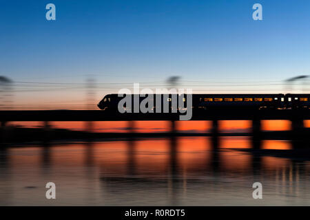 Un LNER treno ad alta velocità (intercity 125) accelerando attraverso il fiume Esk a Mossband (a nord di Carlisle) al tramonto con un deviato east coast in treno. Foto Stock