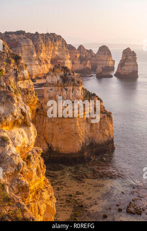 Tramonto sul mare costa rocciosa di arenaria, formazioni rocciose nel mare, Algarve, Lagos, Portogallo Foto Stock