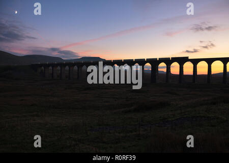 GB classe di merci su rotaie 66 locomotore incrocio viadotto Ribblehead sull'accontentarsi di Carlisle linea ferroviaria con un treno merci che trasportano il cemento sfuso al tramonto Foto Stock