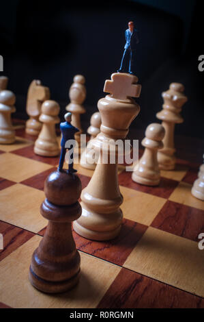 Gli imprenditori in miniatura battaglia con chesspieces gigante per la metafora simbolica Foto Stock