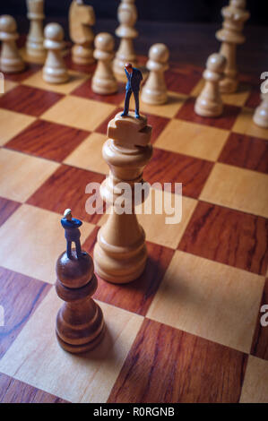 Gli imprenditori in miniatura battaglia con chesspieces gigante per la metafora simbolica Foto Stock