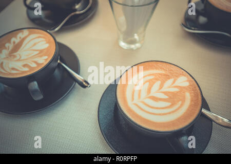 Arte a caldo latte caffè in una tazza sul tavolo di legno e la caffetteria di sfocatura con sfondo bokeh di fondo dell'immagine. Latte Art tavolino vista superiore, felice atmosfera rilassante Foto Stock