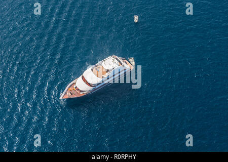 Antenna fuco bird's eye top view foto di yacht di lusso con ponte di legno ormeggiata nel blu profondo delle acque dell'isola di Mykonos, Cicladi Grecia Foto Stock