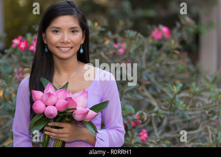 Donna asiatica con fiori di loto bud in posa di fronte a una rosa del deserto tree Foto Stock