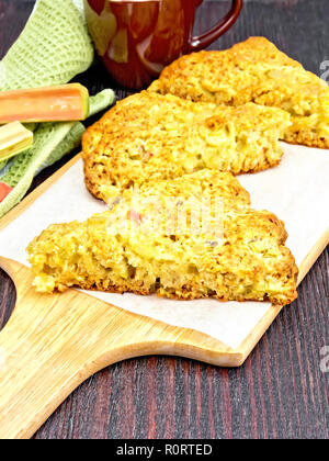 Scones con rabarbaro su pergamena, igienico e vedute di rabarbaro contro lo sfondo del pannello di legno Foto Stock