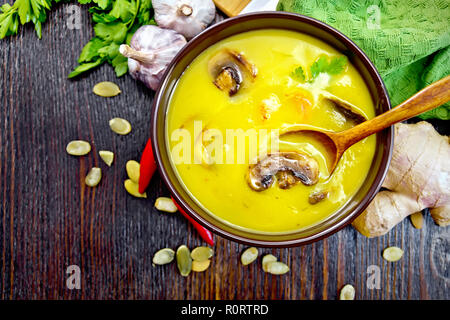 Zuppa di purea di zucca con gamberi e champignon, un cucchiaio in una ciotola marrone, igienico, prezzemolo, semi di zucca, lo zenzero su una tavola di legno sfondo Foto Stock
