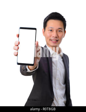 Giovane imprenditore asiatico tenendo un smartphone con schermo vuoto in abito nero Foto Stock