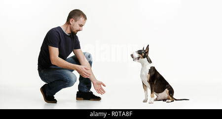 Ritratto emotivo di sorpreso l uomo e il suo cane, il concetto di amicizia e la cura dell'uomo e l'animale. Bull Terrier tipo cane bianco su sfondo per studio. Il concetto di esseri umani ed animali stesse emozioni Foto Stock