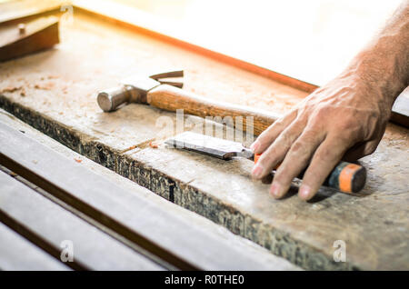 Le mani di un falegname lavora con uno scalpello e un martello sul banco di lavoro in legno Foto Stock