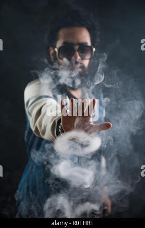 Fumatori vape. vaping uomo tenendo un mod. Gli anelli di Vape. Un uomo lancia un anello di fumo. Trucchi con il fumo. Foto Stock