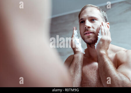 Blue-eyed uomo con bel corpo muscolare la rasatura il suo volto al mattino Foto Stock