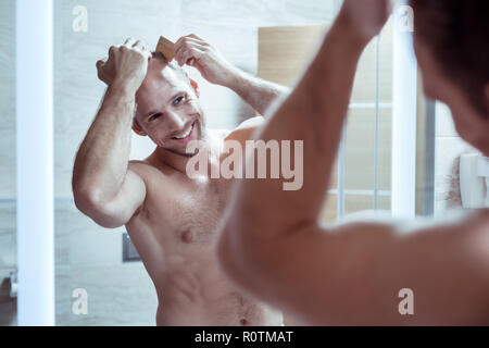 Bel uomo barbuto sensazione allegro mentre pettinare capelli al mattino Foto Stock