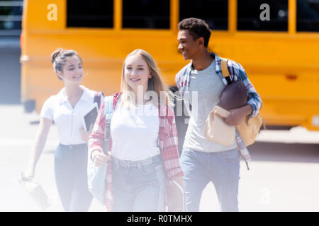 Gruppo di felice teen gli studenti a piedi nella parte anteriore del bus di scuola Foto Stock