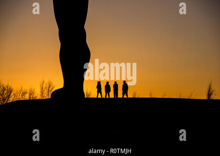 Quattro persone in piedi accanto a un angelo del Nord al tramonto. Foto Stock