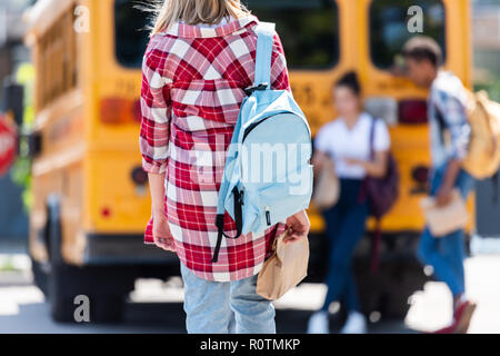 Vista posteriore di teen schoolgirl per raggiungere a piedi i compagni di classe appoggiata sul bus di scuola Foto Stock