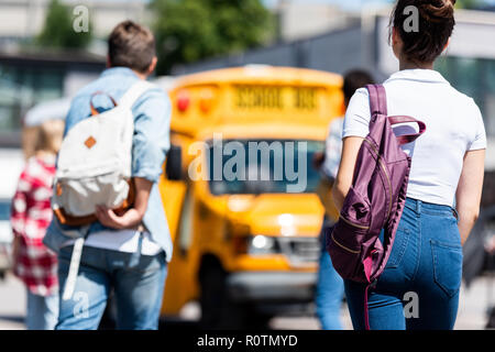 Vista posteriore del gruppo di studenti con zaini a piedi a scuola bus Foto Stock