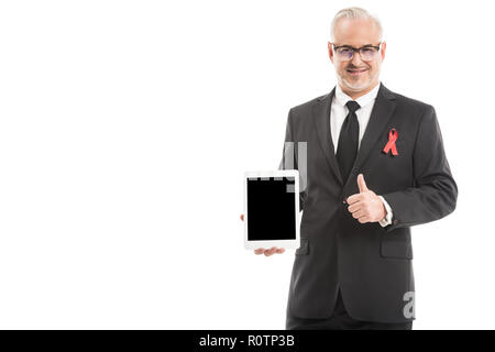 Imprenditore maturo in tuta con la consapevolezza del AIDS red ribbon holding tablet con schermo vuoto e mostrando il pollice in alto isolato su bianco Foto Stock