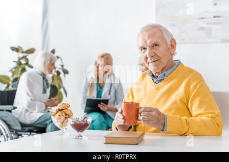 Senior uomo bere il tè mentre medico esaminando le donne anziane Foto Stock