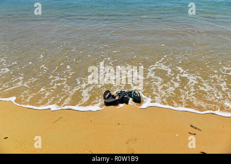 Il mare lambisce un paio di infradito e sandali a sinistra su una spiaggia dorata Foto Stock