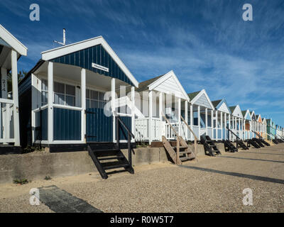 Una fila di vivacemente colorato beach capanne lungo il lungomare di Southwold contro un luminoso cielo blu Foto Stock