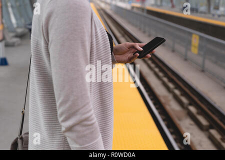 Donna che utilizza il telefono cellulare sulla piattaforma alla stazione ferroviaria Foto Stock