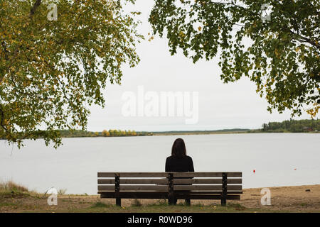 Donna seduta sul banco vicino a Riverside Foto Stock