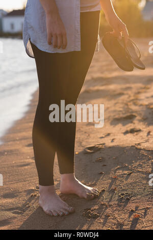 Donna che mantiene le ciabatte sulla spiaggia Foto Stock