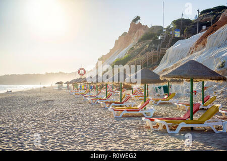 Colorato lettini sotto gli ombrelloni di paglia sulla spiaggia di Falesia, Albufeira Algarve Foto Stock