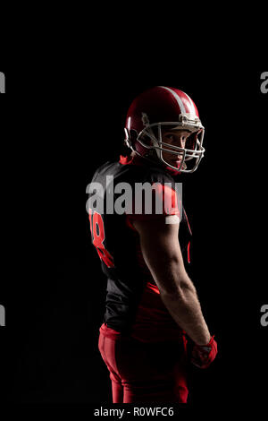 Giocatore di football americano nel casco in piedi su sfondo nero Foto Stock