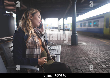 Donna incinta parlando al telefono mobile alla stazione ferroviaria Foto Stock