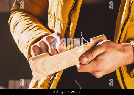 Costruzione o riparazione su legno. Close-up delle mani dell'uomo ruotando il blocco di legno con un coltello speciale. Tonica foto. Messa a fuoco selettiva Foto Stock