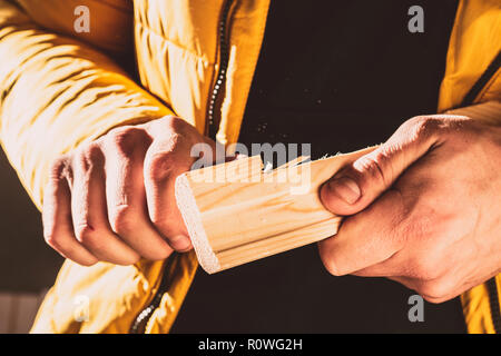 Costruzione o riparazione su legno. Close-up delle mani dell'uomo ruotando il blocco di legno con un coltello speciale. Tonica foto. Messa a fuoco selettiva Foto Stock