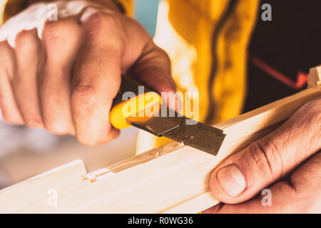 Costruzione o riparazione su legno. Close-up delle mani dell'uomo ruotando il blocco di legno con un coltello speciale. Tonica foto. Messa a fuoco selettiva Foto Stock