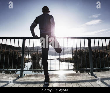 Tall sportivo a riscaldare i suoi muscoli, stirando le sue gambe prima dell'esecuzione di allenamento al mattino. Mattina di sole al di fuori al lago di montagna Foto Stock