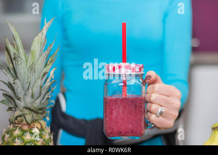 Ragazza con mason jar mug in mano colma di frutti rossi frullato. La donna nella cucina di casa con il suo drink preferito. Detox e cibo sano e bere Foto Stock