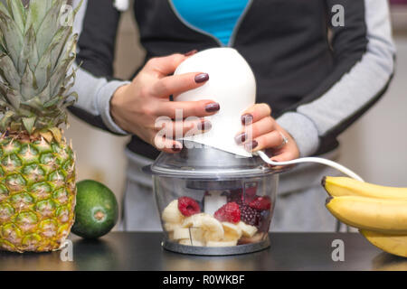 Donna miscelazione di banana, blackberry, mirtilli e lamponi in Blender. Ragazza in casa rendono la cucina frullato sano bere. Sana e detox food Foto Stock
