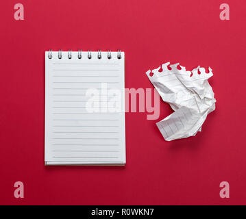 Aprire il notebook con fogli bianchi e una accartocciata strappato da un foglio di carta su uno sfondo rosso Foto Stock