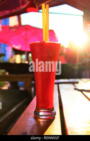 Cerca rinfrescante daiquiri alla fragola bevanda alcolica su un tavolo, scintillanti sotto la luce diretta del sole. Foto Stock