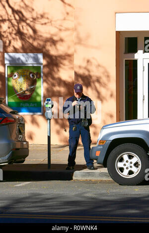 Un maschio di parcheggio enforcement officer scrive digitalmente un biglietto per un veicolo il cui tempo di parcheggio ha elaspsed nel centro cittadino di Santa Fe NM, Stati Uniti d'America Foto Stock