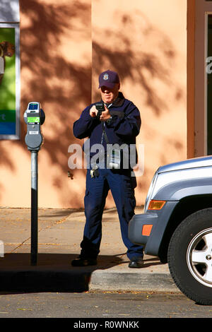 Un maschio di parcheggio enforcement officer scrive digitalmente un biglietto per un veicolo il cui tempo di parcheggio ha elaspsed nel centro cittadino di Santa Fe NM, Stati Uniti d'America Foto Stock