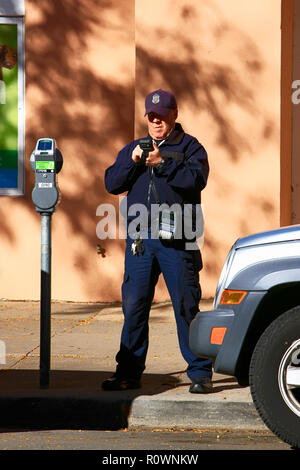 Un maschio di parcheggio enforcement officer scrive digitalmente un biglietto per un veicolo il cui tempo di parcheggio ha elaspsed nel centro cittadino di Santa Fe NM, Stati Uniti d'America Foto Stock