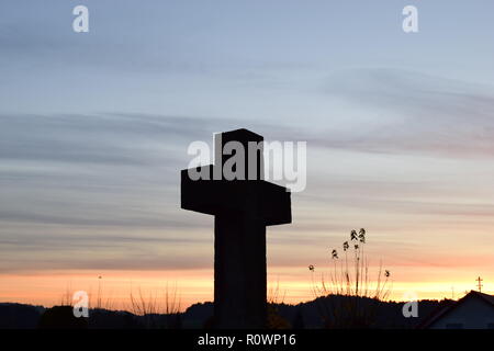 Sequenza temporale della sera Cielo di tramonto visto da dietro una sabbia croce di pietra scultura durante il sole al tramonto nel cimitero civile Reimsbach, Saarland, Foto Stock