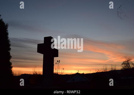 Sequenza temporale della sera Cielo di tramonto visto da dietro una sabbia croce di pietra scultura durante il sole al tramonto nel cimitero civile Reimsbach, Saarland, Foto Stock