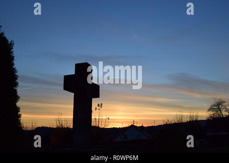 Sequenza temporale della sera Cielo di tramonto visto da dietro una sabbia croce di pietra scultura durante il sole al tramonto nel cimitero civile Reimsbach, Saarland, Foto Stock