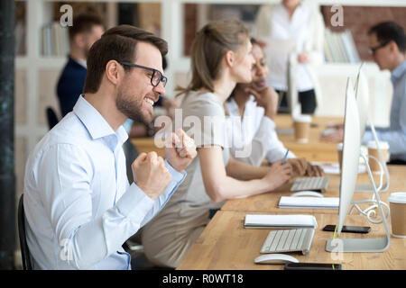 Maschio eccitato dipendente sente euforici la lettura di buone notizie on line Foto Stock