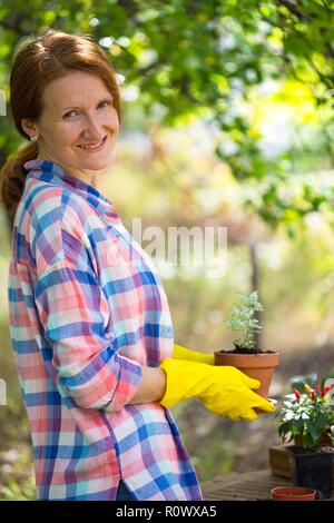 Ragazza sorridente trapianti fiori nel giardino. vasi da fiori e piante per il trapianto Foto Stock