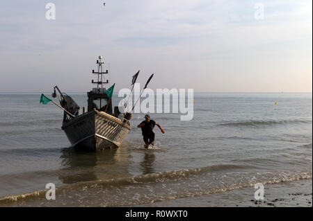 Pescatore che costeggia la sua barca attorno alla terra sulla spiaggia, Normandia, Francia Foto Stock