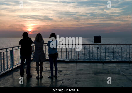 Tre donne a fotografare il tramonto dal traghetto attraverso la Manica, silhouette Foto Stock