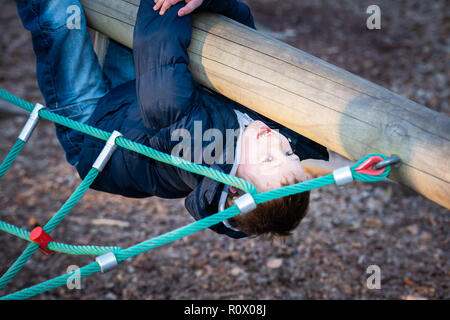 Un simpatico atletico ragazzino pratica con la sua abilità di arrampicata su una piccola parete di arrampicata in Colchester pubblico Country Park Foto Stock